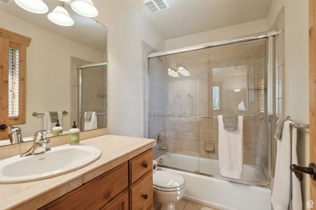 Full bath featuring toilet, vanity, shower / bath combination with glass door, and tile patterned flooring | Image 40