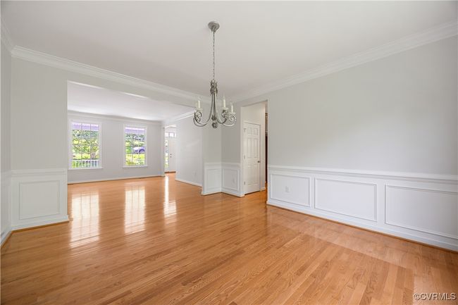 Unfurnished dining area featuring ornamental molding, light wood finished floors, a decorative wall, and a chandelier and view of living room | Image 13