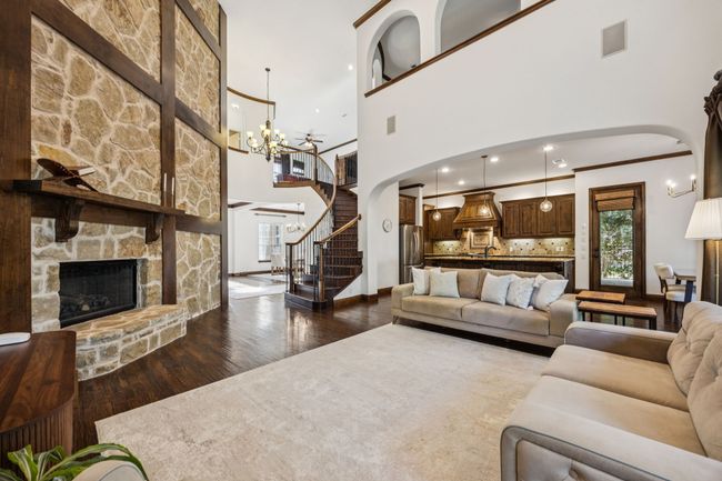 Living room with arched walkways, dark wood-type flooring, stairway, a high ceiling, and a stone fireplace | Image 15