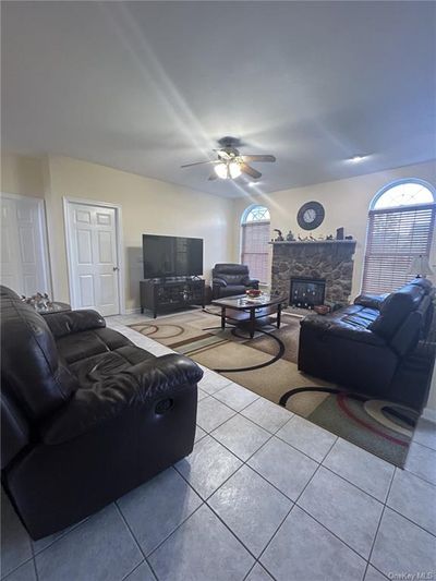 Tiled living room with ceiling fan, a stone fireplace, and a wealth of natural light | Image 2