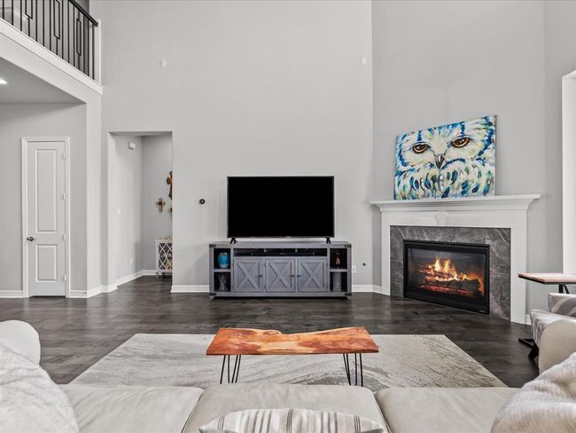 The living room open to the kitchen features wood flooring, two-story high ceilings, a wall of windows and a cozy fireplace for those cold winter nights | Image 5