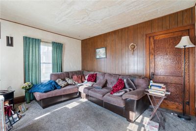 Living room with wood walls, carpet, and a textured ceiling | Image 3