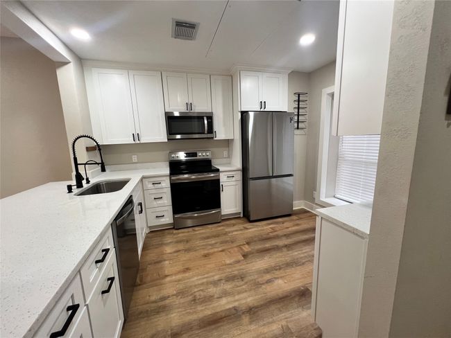Kitchen with appliances with stainless steel finishes, a sink, wood finished floors, white cabinets, and recessed lighting | Image 12