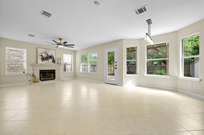 Unfurnished living room with healthy amount of natural light, tile patterned flooring, ceiling fan, and a fireplace with raised hearth | Image 12