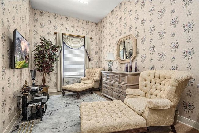 This is an elegantly furnished sitting area of the suite with floral wallpaper, traditional furniture, and a large window with classic drapery, creating a cozy and vintage ambiance. | Image 16