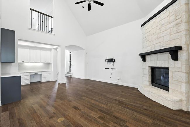 Unfurnished living room with a stone fireplace, ceiling fan, high vaulted ceiling, built in study area, and dark wood-style flooring | Image 10