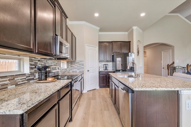 Kitchen featuring appliances with stainless steel finishes, a sink, dark brown cabinets, arched walkways, and a kitchen island with sink | Image 10