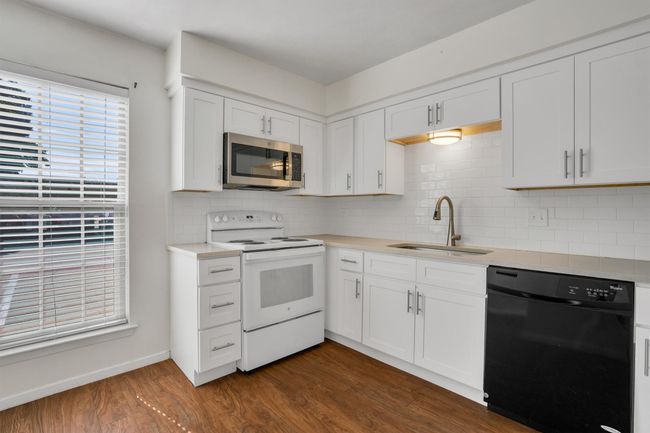 Kitchen featuring black dishwasher, electric range, stainless steel microwave, dark wood-style flooring, and light countertops | Image 11