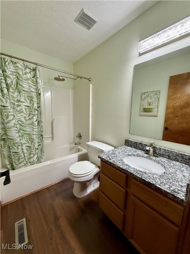 Bathroom with wood finished floors, shower / bath combo with shower curtain, granite vanity, toilet, and a textured ceiling | Image 29