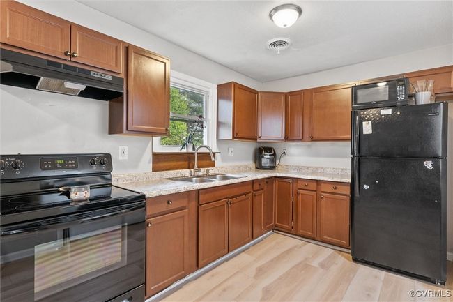 Kitchen featuring a sink, under cabinet range hood, light wood-type flooring, black appliances, and visible vents | Image 16