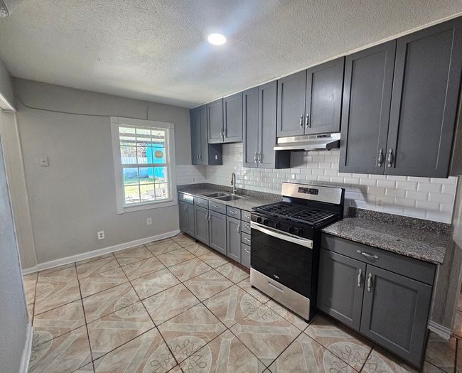 Kitchen with stainless steel range with gas cooktop, under cabinet range hood, tasteful backsplash, a textured ceiling, and gray cabinetry | Image 27