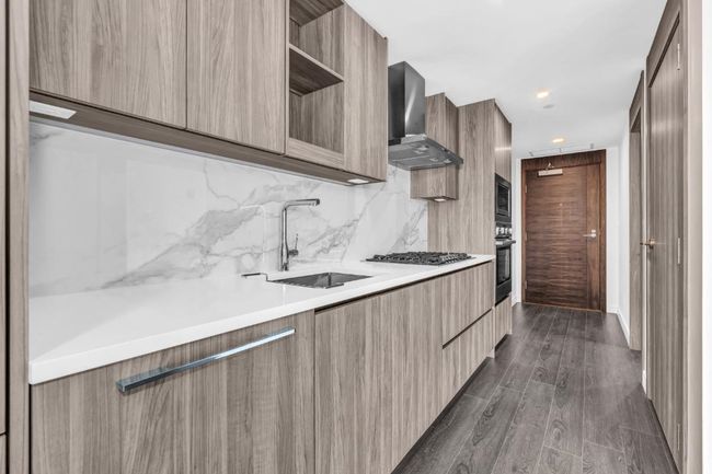 Kitchen featuring modern cabinets, wall chimney exhaust hood, light countertops, stainless steel appliances, and backsplash | Image 4