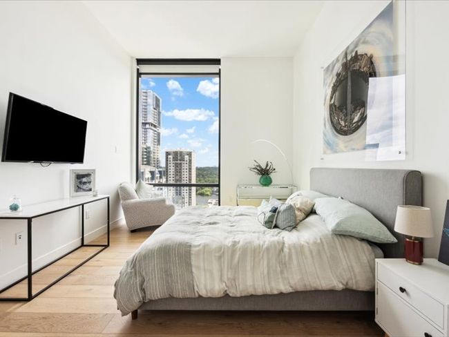 Bedroom featuring expansive windows, light wood-type flooring, baseboards, and a view of city | Image 6