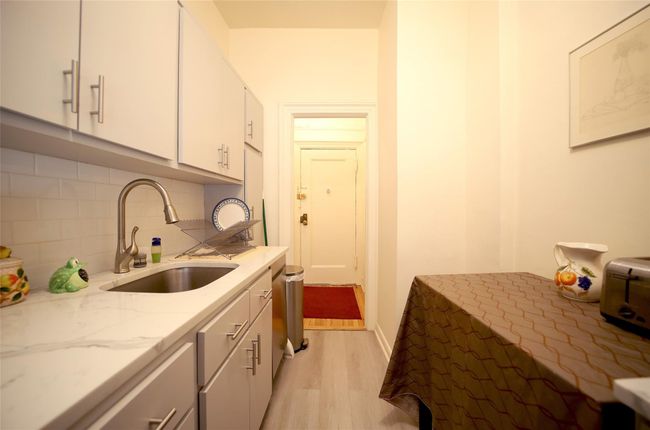 Kitchen with a sink, light wood-style flooring, tasteful backsplash, light stone countertops, and white cabinetry | Image 8