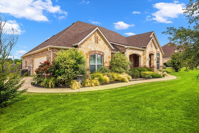 View of front of house featuring stone siding, a garage, a front yard, a shingled roof, and brick siding | Image 4