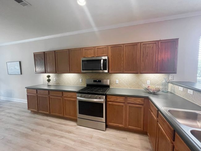 Kitchen featuring appliances with stainless steel finishes, crown molding, brown cabinets, decorative backsplash, and light wood finished floors | Image 7