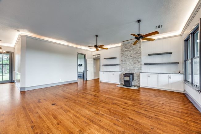Unfurnished living room with a wood stove, ornamental molding, light wood-style floors, ceiling fan, and a chandelier | Image 9