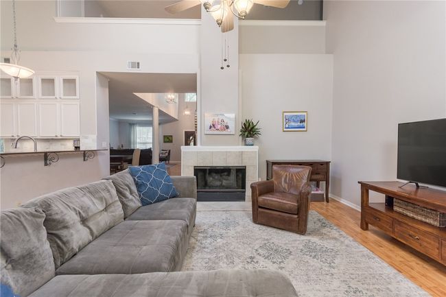 Living area featuring a ceiling fan, light wood-style flooring, a high ceiling, and a tile fireplace | Image 10