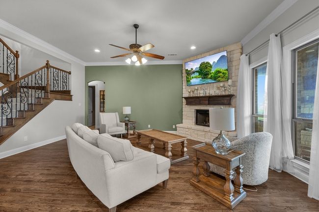 Living area featuring ornamental molding, a stone fireplace, ceiling fan, wood finished floors, and arched walkways | Image 9