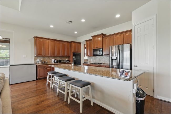 Kitchen with freestanding refrigerator, brown cabinetry, a chandelier, light stone counters, and recessed lighting | Image 12