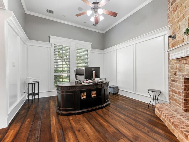 Office area featuring a decorative wall, a ceiling fan, dark wood finished floors, ornamental molding, and a brick fireplace | Image 13