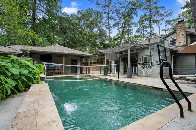 This backyard features a spacious pool with a removable basketball hoop and volleyball net, surrounded by lush greenery. There's a cozy patio area with a pergola and ample seating, perfect for outdoor entertaining. | Image 39