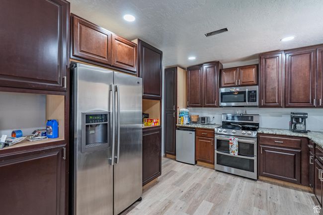 Kitchen featuring appliances with stainless steel finishes, light wood finished floors, light stone counters, dark brown cabinetry, and recessed lighting | Image 24