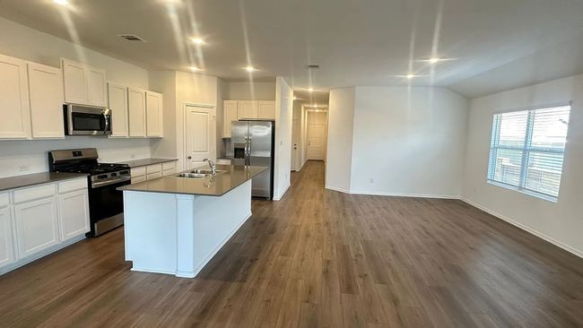 Kitchen with appliances with stainless steel finishes, dark countertops, a kitchen island with sink, dark wood finished floors, and white cabinetry | Image 8