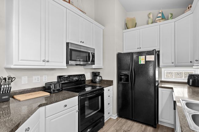 Kitchen with light wood finished floors, dark countertops, a sink, and black appliances | Image 25