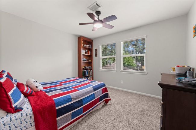 This secondary bedroom features cozy carpeting, a ceiling fan, and ample natural light from two windows. | Image 31
