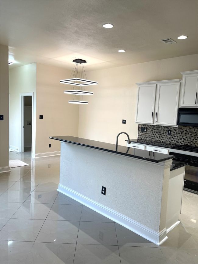 Kitchen with dark countertops, black microwave, oven, decorative backsplash, and white cabinets | Image 8