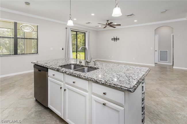 Kitchen with dishwasher, hanging light fixtures, a center island with sink, white cabinetry, and light tile floors | Image 6