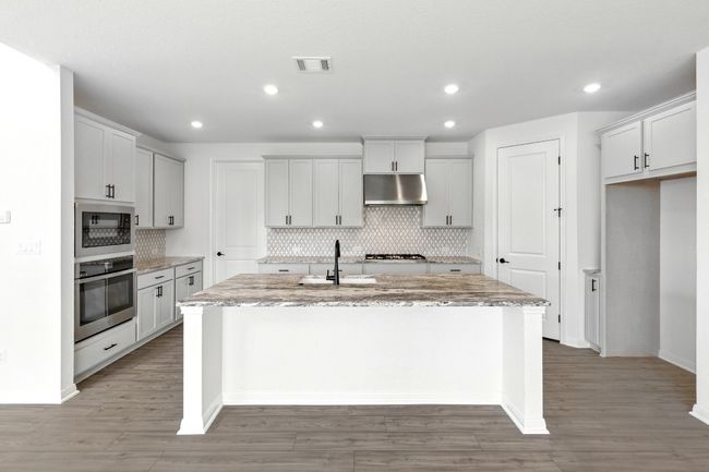 Kitchen featuring appliances with stainless steel finishes, under cabinet range hood, an island with sink, tasteful backsplash, and light stone counters | Image 10