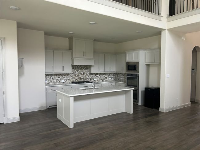 Kitchen featuring appliances with stainless steel finishes, tasteful backsplash, a sink, a center island with sink, and dark wood-style floors | Image 5
