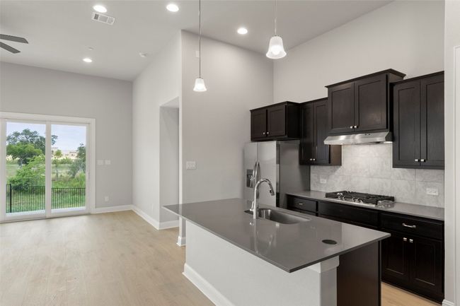 Kitchen with backsplash, light wood-style flooring, a kitchen island with sink, appliances with stainless steel finishes, and pendant lighting | Image 19