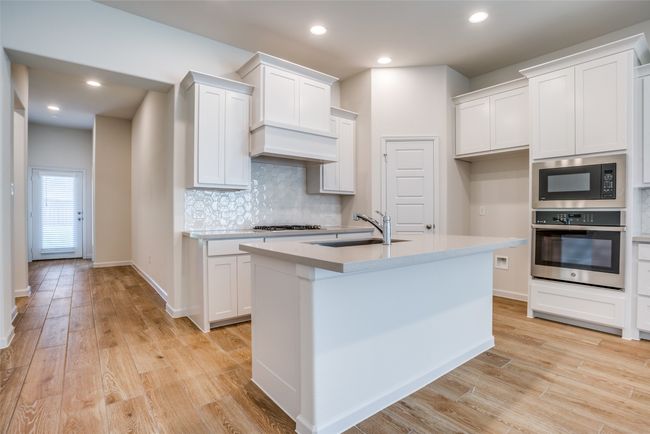 Kitchen featuring stainless steel appliances, a sink, tasteful backsplash, light wood finished floors, and light countertops | Image 10