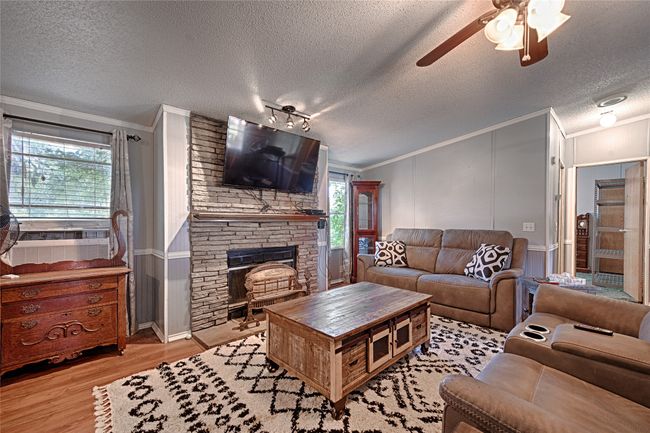 Living area featuring ornamental molding, light wood-style floors, a textured ceiling, a stone fireplace, and a ceiling fan | Image 8