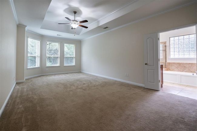 Spare room featuring light carpet, a tray ceiling, a ceiling fan, and crown molding | Image 10