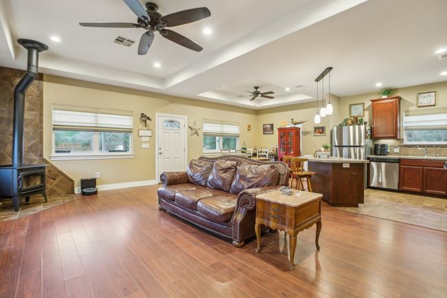 Living room with a wood stove, sink, ceiling fan, a raised ceiling, and light hardwood / wood-style​​‌​​​​‌​​‌‌​‌‌​​​‌‌​​‌‌​‌​​​​​‌ flooring | Image 6