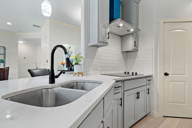 Kitchen featuring ornamental molding, backsplash, wall chimney range hood, light stone countertops, and black electric cooktop | Image 15
