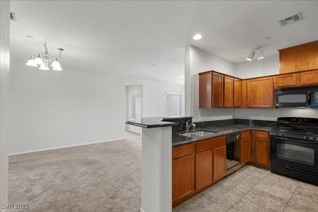 Kitchen featuring black appliances, a chandelier, brown cabinets, light colored carpet, and dark stone counters | Image 12
