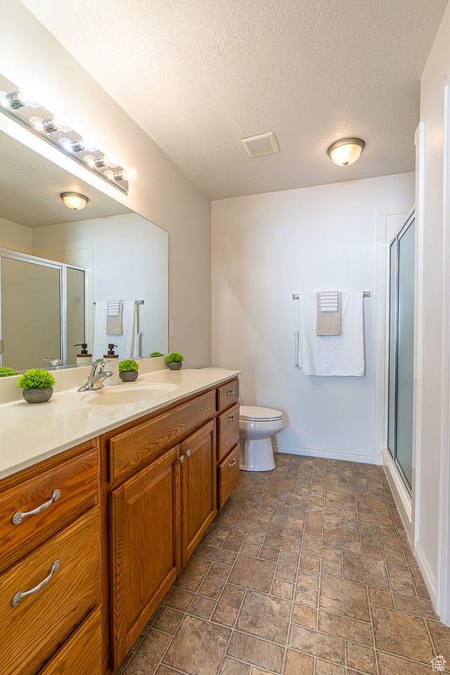 Full bath with a textured ceiling, visible vents, a shower stall, toilet, and vanity | Image 18