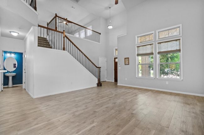 Unfurnished living room with stairs, a towering ceiling, wood finished floors, and baseboards | Image 12