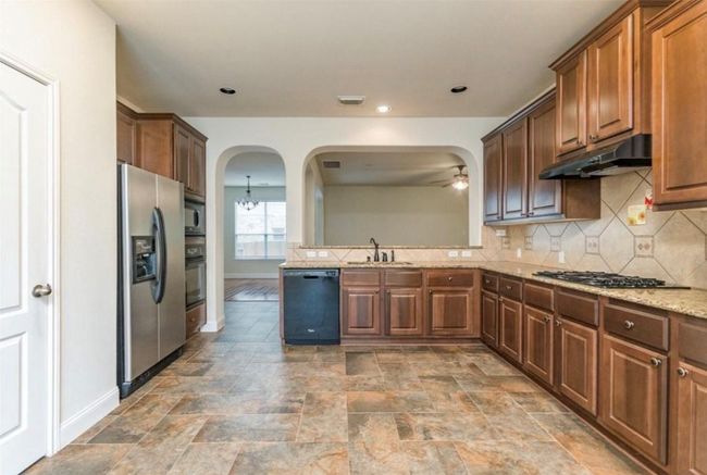 Kitchen featuring black appliances, under cabinet range hood, ceiling fan, arched walkways, and stone finish flooring | Image 8