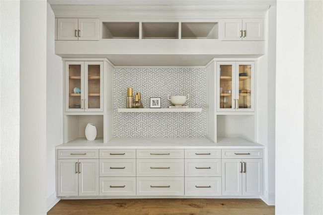 This beautifully designed butler’s pantry serves as a seamless transition between the kitchen and dining room. Topped with luxurious Opal White Satin Marble, the space is complemented by custom cabinetry, glass-front display shelves, and ample storage, combining both elegance and functionality for effortless entertaining. | Image 32