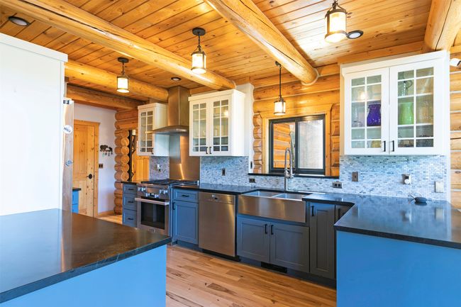 Kitchen with appliances with stainless steel finishes, a sink, dark countertops, wooden ceiling with exposed beams, and rustic walls | Image 8