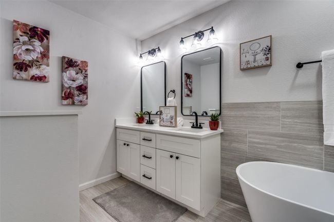 Bathroom featuring double vanity, a soaking tub, tile walls, light wood-style floors, and a textured wall | Image 18