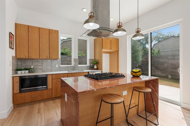 Kitchen with black appliances, light wood finished floors, backsplash, a kitchen island, and a sink | Image 7