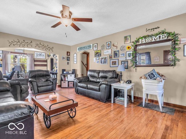 living room featuring a textured ceiling, light hardwood flooring, ceiling fan, arched walkways, and wide baseboards | Image 4