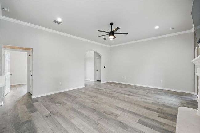 Unfurnished living room with ceiling fan, arched walkways, baseboards, crown molding, and light wood finished floors | Image 8